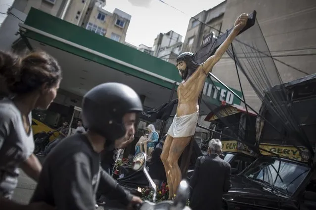 A couple on a motorbike rides past cars with statues of Jesus Christ mounted on the bonnet in Beirut, Lebanon, 29 April 2016. To mark Orthodox Good Friday cars with oversized statues of Jesus Christ are driving through the Christian neighborhoods of Beirut playing religious music and prayers. (Photo by Oliver Weiken/EPA)