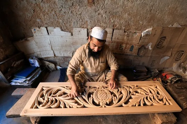 A carpenter uses sandpaper on a wooden panel after carving it at a workshop in Peshawar, Pakistan on February 10, 2022. (Photo by Fayaz Aziz/Reuters)
