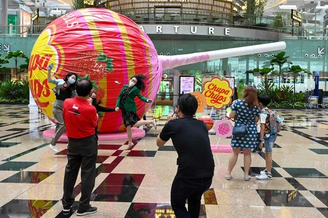 People pose for pictures in front a giant lollipop candy display in the departure hall of Changi International Airport in Singapore on March 11, 2022. (Photo by Roslan Rahman/AFP Photo)