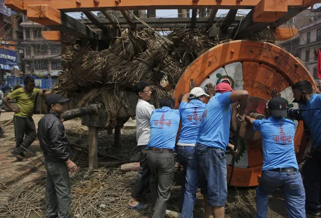 In this April 21, 2017 photo, members of the Barahi community assemble the Rato Machindranath Chariot in Lalitpur, Nepal. The Barahis are responsible for repairing the giant wheels, carving the base and erecting the tower of logs for the chariot. The wooden chariot is built to appease the gods in hopes of being blessed with a good rainfall followed by a bountiful harvest. (Photo by Niranjan Shrestha/AP Photo)