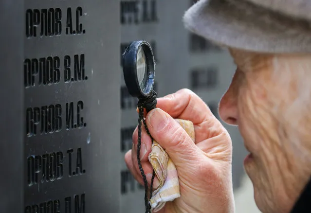 In this photo, taken on October 30, 2019 in Smolensk Region, Russia, Maria Orlova looks for her father Vasily Orlov executed in 1938, on the Wall of Memory bearing the names of the victims of political repressions interred at the Katyn Memorial outside Smolensk. A ceremony to rebury the remains of 559 Soviet citizens discovered by search teams here this summer takes on October 30, Day of Remembrance of Political Repression Victims. (Photo by Natalia Fedosenko/TASS)