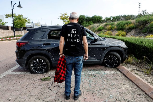 A man looks at a car that was damaged by shrapnel after a rocket that was launched from Gaza landed nearby, near Ashkelon in southern Israel on May 3, 2023. (Photo by Amir Cohen/Reuters)