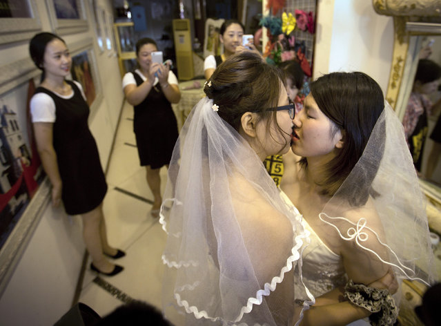 In this July 2, 2015, file photo, Teresa Xu, left, and Li Tingting, right, share a kiss as clerks take photographs in a beauty salon where the two were preparing for their wedding in Beijing. LGBT activists in China are seeking to legalize same-s*x marriage through a novel tactic: submitting opinions on a draft new civil code to the country’s legislature. (Photo by Mark Schiefelbein/AP Photo/File)