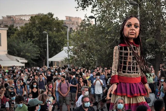 Members of the public gather as “Little Amal”, a giant puppet depicting a young refugee girl, is paraded through the streets of Athens, as the ancient Acropolis is seen in the background, on September 2, 2021. The 3,5 meter-tall puppet of a Syrian refugee girl is on a journey from Turkey, crossing through Greece, Italy, France, Switzerland, Germany, Belgium and finally to the UK, as part of the initiave “The Walk”, aimed at creating awareness on the urgent needs of young refugees. (Photo by Louisa Gouliamaki/AFP Photo)