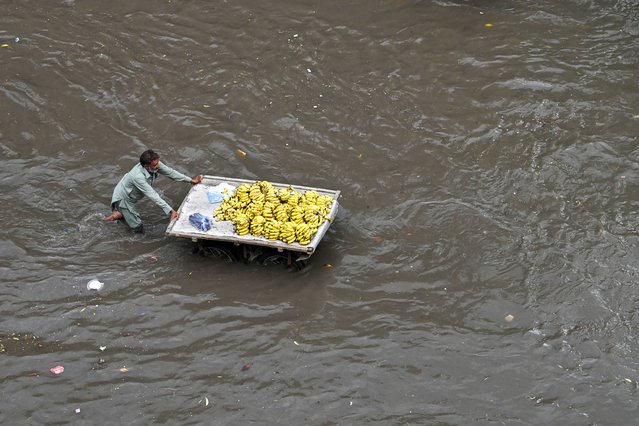 A fruit seller pushes his cart of bananas through a flooded street after heavy rains in Lahore on July 12, 2024. (Photo by Arif Ali/AFP Photo)