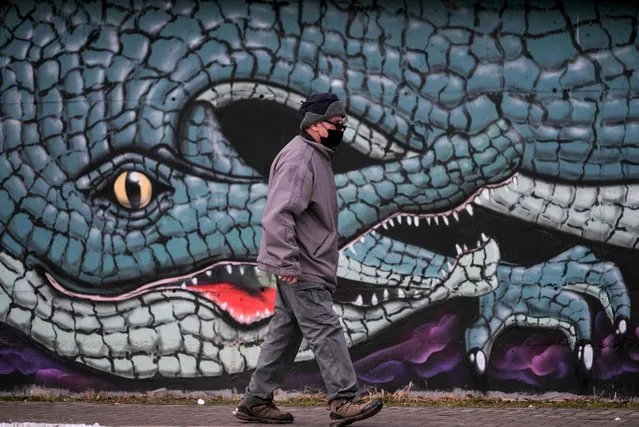 A man wearing a protective face mask walks past a graffiti in Pristina on January 21, 2022. (Photo by Armend Nimani/AFP Photo)