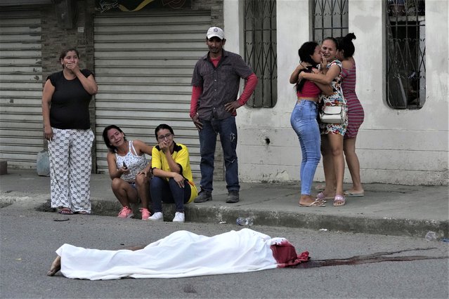 Persons grieve near the body of a man, killed in unknown circumstances, on a street in Duran, Ecuador, Friday, July 21, 2023. Ecuador is gripped by a serious outbreak of violence that authorities attribute to disputes among organized crime groups. (Photo by Dolores Ochoa/AP Photo)