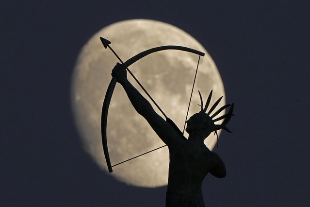 The bronze sculpture of “Ad Astra” a Kansa Indian, perched atop the Kansas State Capitol dome is silhouetted against the waxing moon, Monday, October 14, 2024, in Topeka, Kan. (Photo by Charlie Riedel/AP Photo)