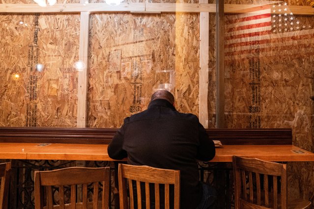 A person eats inside a restaurant with plywood covering the windows near the White House in  Washington on November 4, 2024. (Photo by Nathan Howard/Reuters)