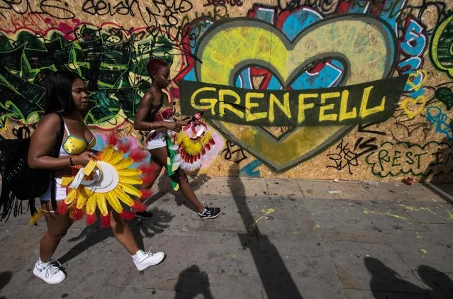 Two performers walk past a piece of graffiti relating to the Grenfell tower tragedy during the Notting Hill Carnival parade on August 28, 2017 in London, England. The Notting Hill Carnival has taken place since 1966 and now has an attendance of over two million people. (Photo by Chris J. Ratcliffe/Getty Images)