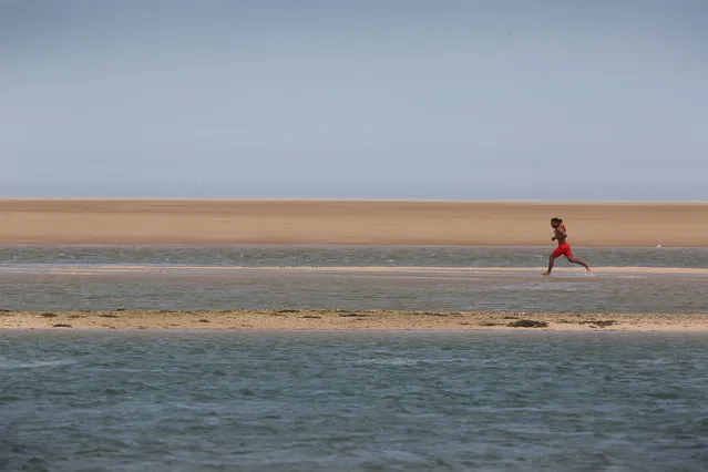 A lifeguard rushes to warn sunbathers that the tide is encircling them on July 11, 2022 in Wells-next-the-Sea, United Kingdom. Britain will experience a heatwave this week as temperatures in some parts are expected to reach 30c. A level 2 heat health warning has been issued of the south and easten parts of England. (Photo by Martin Pope/Getty Images)