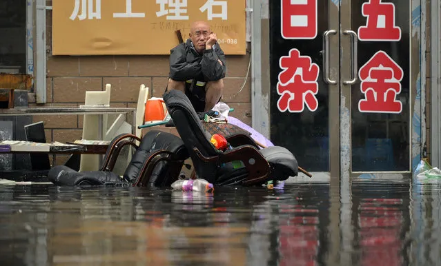 In this Thursday, July 21, 2016 photo, a man sits outside of a flooded shop in Shenyang in northeastern China's Liaoning Province. (Photo by Chinatopix via AP Photo)