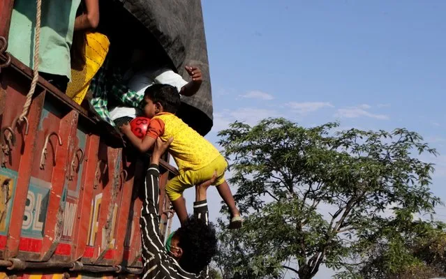 A migrant workers family desperate to reach their home in neighboring Madhya Pradesh state hitchhike behind a truck that will take them to the outskirts of the city in Mumbai, India, Monday, May 11, 2020. India's train network, closed in late March, will gradually restart operations on Tuesday as the country eases its coronavirus lockdown amid a steep rise in the cases of infections. (Photo by Rajanish Kakade/AP Photo)