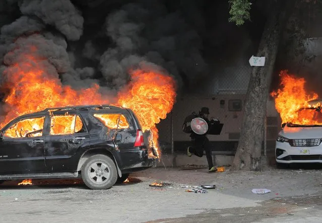 A man runs with looted goods near cars on fire during protests over rising fuel prices and crime as inflation surged to its highest in a decade, in Port-au-Prince, Haiti on September 14, 2022. (Photo by Ralph Tedy Erol/Reuters)