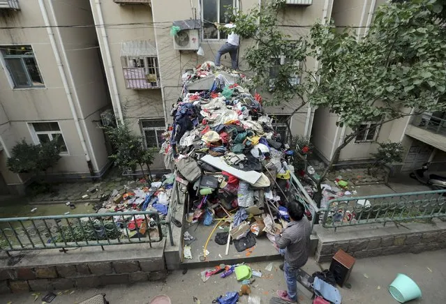 A pile of garbage is seen blocking an entrance to a residential building as workers clean up one of its apartments, in Qingdao, Shandong province, China, September 9, 2015. According to local media, authorities have started cleaning out the apartment of an elderly woman, with the help of her son. The authorities were acting on persistent complaints from the surrounding residents due to the woman's collection and storage of trash in her home. (Photo by Reuters/Stringer)