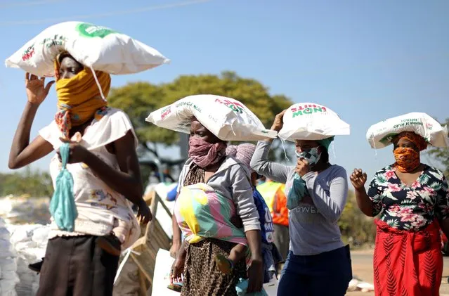 Women carry bags of maize meal on their heads as people queue to receive food aid amid the spread of the coronavirus disease (COVID-19) outbreak, at the Itireleng informal settlement, near Laudium suburb in Pretoria, South Africa, May 20, 2020. (Photo by Siphiwe Sibeko/Reuters)