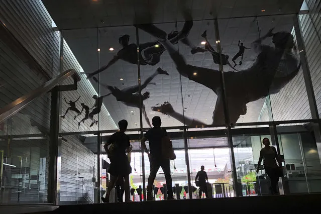 People are silhouetted as they enter a subway station where the glass entrance is decorated with decals of athletes in action on Monday, November 13, 2017 in Singapore. Singapore's rail system is one of the most popular and efficient ways for commuters to get around the city-state. (Photo by Wong Maye-E/AP Photo)