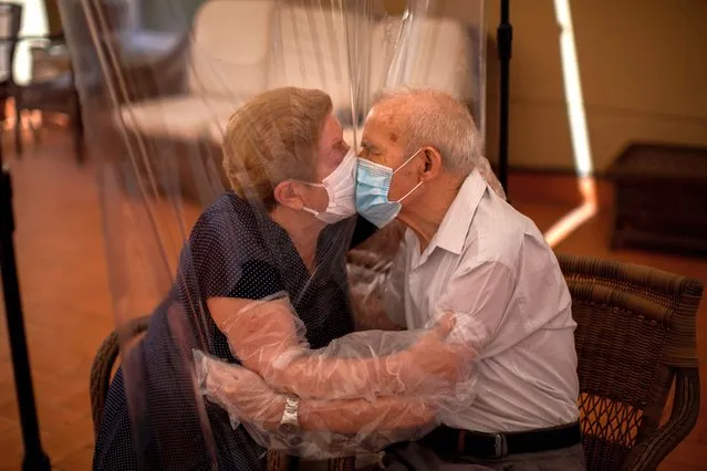 Agustina Cañamero, 81, and Pascual Pérez, 84, hug and kiss through a plastic film screen to avoid contracting the new coronavirus at a nursing home in Barcelona, Spain, Monday, June 22, 2020. The Ballesol Fabra i Puig elderly care center installed the screens to resume relatives' visits to residents 102 days after a strict, nationwide lockdown separated them. As she and her husband broke out into tears while kissing through layers of protective masks and the transparent plastic film, Cañamero said that the couple had never spent such long time with no physical contact in 59 years of marriage. Nursing homes in Spain have been particularly hit by the novel virus, which has claimed at least 28,300 lives nationwide. (Photo by Emilio Morenatti/AP Photo)