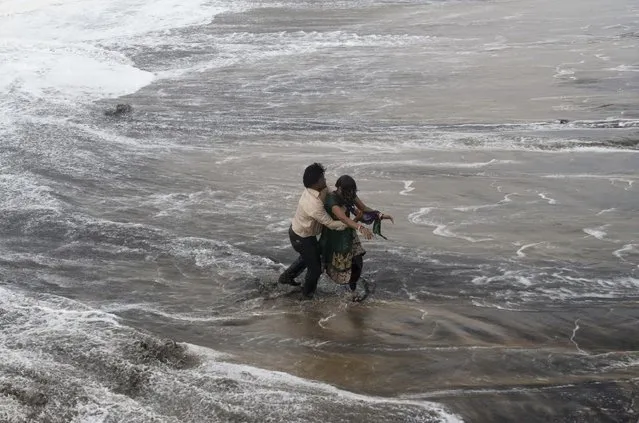 A man, left rescues a woman who fell in water due to strong tidal waves prior to a cyclone on the Bay of Bengal coast at Gopalpur, Orissa, about 285 kilometers (178 miles) north east of Visakhapatnam, India, Sunday, October 12, 2014. (Photo by Biswaranjan Rout/AP Photo)