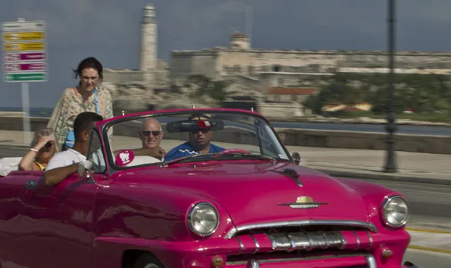In this October 15, 2014 photo, tourists ride in a classic American car on the Malecon in Havana, Cuba. Those lucky enough to have a pre-revolutionary car can earn money legally by ferrying tourists – or Cubans celebrating weddings – along Havana's waterfront Malecon boulevard. (Photo by Franklin Reyes/AP Photo)