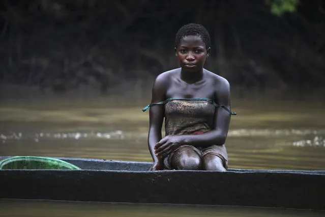 A young woman named Akpomene is pictured coated in oil stains as she sits in a canoe near river Nun in Nigeria's oil state of Bayelsa November 27, 2012. Akpomene fishes in the creek and sells the fish to help her family. She washes after fishing but has sticky rashes on her body. (Photo by Akintunde Akinleye/Reuters)