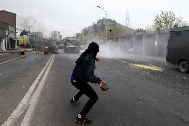 A demonstrator prepares to throw a stone toward riot police vehicles during a protest marking the country's 1973 military coup in Santiago, Chile September 11, 2016. (Photo by Ivan Alvarado/Reuters)