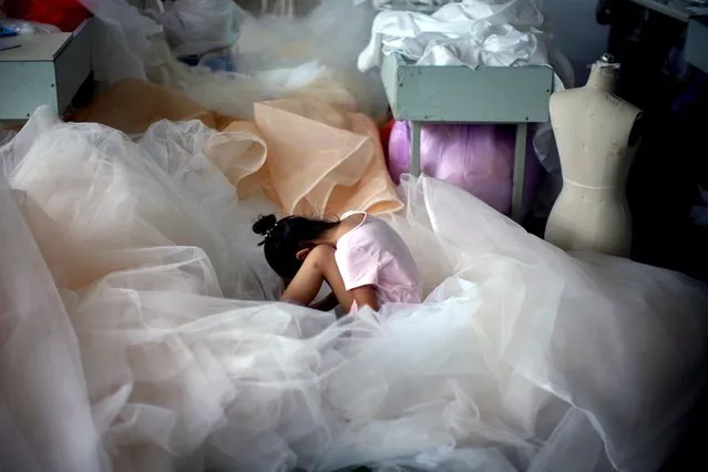 A girl sits on a piece of fabric as she plays on a mobile phone at a small wedding dress factory, during the coronavirus disease (COVID-19) outbreak, in Suzhou, Jiangsu province, China, July 23, 2020. (Photo by Aly Song/Reuters)