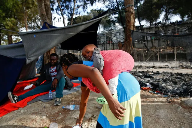 A migrant woman carries a baby as she stands next to the remains of a burned tent at the Moria migrant camp, after a fire that ripped through tents and destroyed containers during violence among residents, on the island of Lesbos, Greece, September 20, 2016. (Photo by Giorgos Moutafis/Reuters)