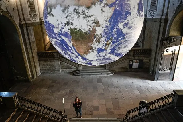 A visitor looks up at the artwork “Gaia” created by British visual artist Luke Jerram on display at the Royal Palace's south vault in Stockholm on December 12, 2022. The “Gaia” globe measures seven meters in diameter and was created from images taken from NASA photographs of the Earth's surface. It is one of 22 works of art that illuminate Stockholm during light festival “Nobel Week Lights”. (Photo by Anders Wiklund/TT News Agency/AFP Photo)