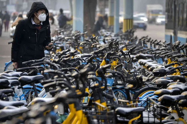 A man wearing a face mask uses his smartphone to unlock a rental bicycle during the morning rush hour in Beijing, Friday, February 10, 2023. (Photo by Mark Schiefelbein/AP Photo)
