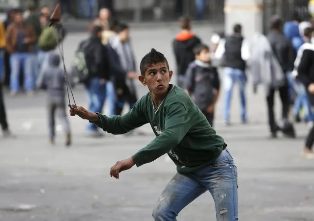 A Palestinian protester uses a sling to hurl stones at Israeli troops following a protest demanding Israel return the bodies of Palestinians who allegedly stabbed Israelis, in the West Bank city of Hebron November 4, 2015. (Photo by Mussa Qawasma/Reuters)