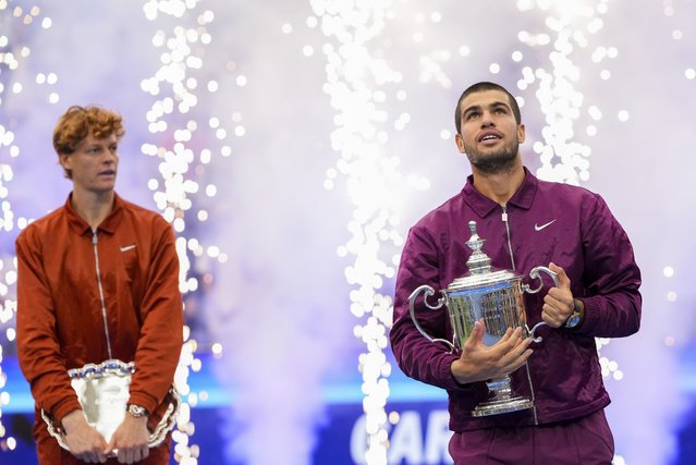 Carlos Alcaraz, of Spain, holds the championship trophy as Jannik Sinner, of Italy, looks on after Alcaraz defeated Sinner in the men's singles final of the U.S. Open tennis championships, Sunday, September 7, 2025, in New York. (Photo by Kirsty Wigglesworth/AP Photo)