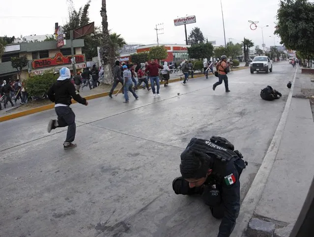 An injured federal police officer (bottom R) is seen as people chase after a car which reversed away after running over civilians, federal police officers, and journalists, during clashes in Chilpancingo, Guerrero, December 14, 2014. (Photo by Jorge Dan Lopez/Reuters)