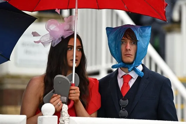 Racegoers shelter from the rain as they attend on the second day of the Grand National Festival horse race meeting at Aintree Racecourse in Liverpool, north-west England, on April 14, 2023. (Photo by Oli Scarff/AFP Photo)