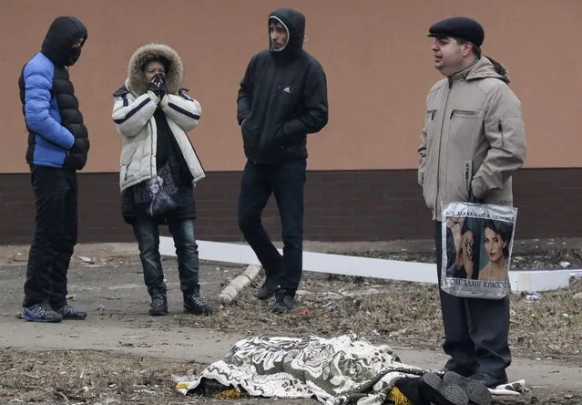 Local residents react as they stand near the covered body of man, who was killed during shelling in the eastern Ukrainian city of Mariupol, 24 January 2015. (Photo by Sergey Vaganov/EPA)