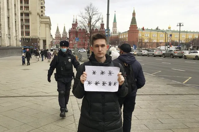 Police officers, left, prepare to detain Dmitry Reznikov holding a blank piece of paper with eight asterisks that could have been interpreted as standing for “No to war” in Russian, with the Kremlin in the background in Moscow, Russia, on Sunday, March 13, 2022. A court found him guilty of discrediting the armed forces and fined him 50,000 rubles ($618) for holding the sign in a demonstration that lasted only seconds before police seized him. (Photo by SOTA via AP Photo)