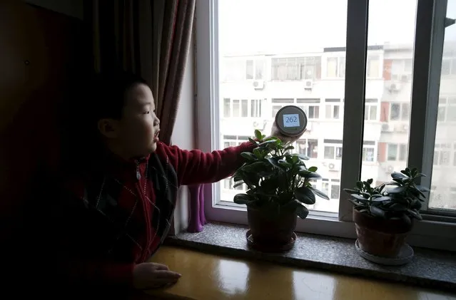 Jiang Zhen's son Doudou checks the air quality outside the window of his room with a portable device measuring air quality during an interview with Reuters in his home, on the second day after China's capital Beijing issued its second ever “red alert” for air pollution, in Beijing, China, December 20, 2015. (Photo by Kim Kyung-Hoon/Reuters)