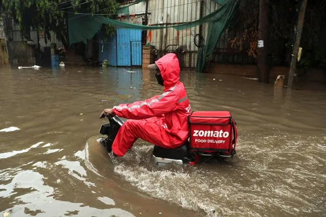 A food delivery person wades through a flooded street after heavy rains in New Delhi, India on July 8, 2023. (Photo by Anushree Fadnavis/Reuters)