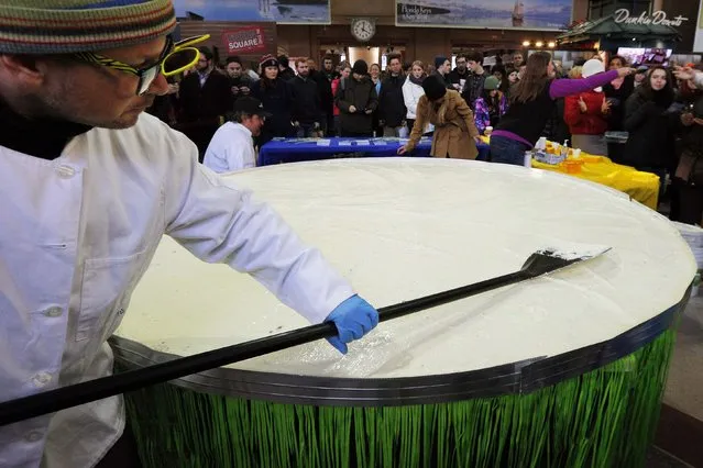 Chef Marky Pierson spreads the filling in what is billed as the world's largest Key lime pie at South Station in Boston, Massachusetts February 5, 2015. The chefs say that the pie, eight feet wide and estimated to weigh 1000 pounds, includes the juice of 5760 Key limes, 200 pounds of graham crackers and 55 gallons of sweetened condensed milk. (Photo by Brian Snyder/Reuters)