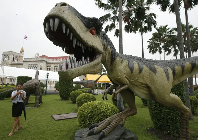 A government official takes a souvenir photo of a scale model of a dinosaur which was set up to decorate the National Children's Day on the compound of the Government House (background), as preparations for the event are going on, in Bangkok, Thailand, 08 January 2016. A variety of dinosaur models is many sizes are hoped to attract and entretain some several hundreds of young Thai children who are expected  to visit the venue on the National Children's Day on 09 January 2016. This annual event in Thailand acknowledges the rights of children. (Photo by Narong Sangnak/EPA)