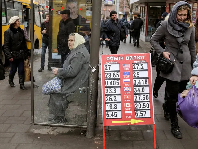 A woman waits for a bus at a bus stop near a currency exchange office in central Lviv, Ukraine, November 25, 2016. (Photo by Gleb Garanich/Reuters)