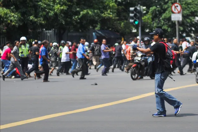In this photo released by China's Xinhua News Agency, an unidentified man with a gun walks in the street as people run in the background on Thamrin street near Sarinah shopping mall in Jakarta, Indonesia, Thursday, January 14, 2016. Suicide bombers exploded themselves in downtown Jakarta on Thursday while gunmen attacked a police post nearby, a witness told The Associated Press. Local television reported more explosions in other parts of the city. (Photo by Veri Sanovri/Xinhua via AP Photo)
