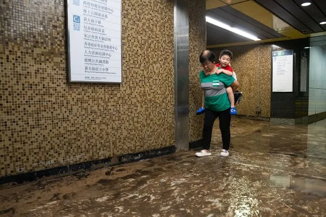 A child is carried over the muddy floor of the Wong Tai Sin MTR station in Hong Kong on September 8, 2023. (Photo by Bertha Wang/AFP Photo)