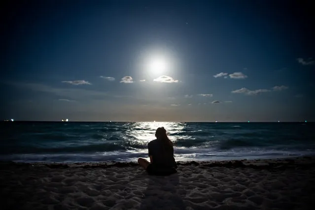 A Super Pink Full Moon lights up the sky as people relax on the beach in Miami Beach on April 26, 2021. (Photo by Chandan Khanna/AFP Photo)