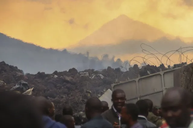 Residents check the damages caused by lava from the overnight eruption of Mount Nyiragongo, seen in background, in Buhene, on the outskirts of Goma, Congo in the early hours of Sunday, May 23, 2021. (Photo by Justin Kabumba/AP Photo)