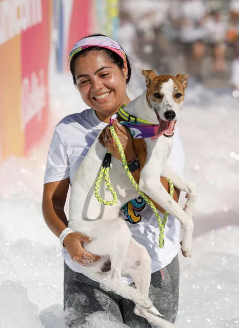 A participant carries her pet dog as she runs through a foam bath during the “Colour My Run” charity fun run in Ta' Xbiex, Malta on October 15, 2023. (Photo by Darrin Zammit Lupi/Reuters)