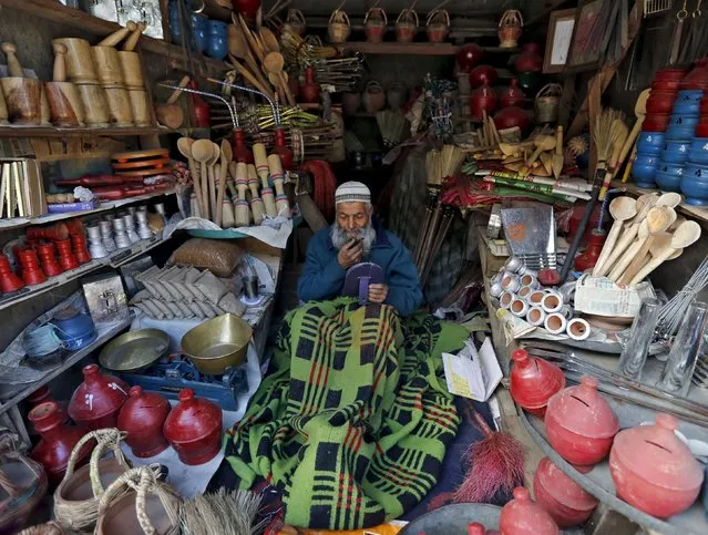 A Kashmiri man, sitting covered with a blanket, trims his beard inside his shop in Srinagar February 1, 2016. (Photo by Danish Ismail/Reuters)