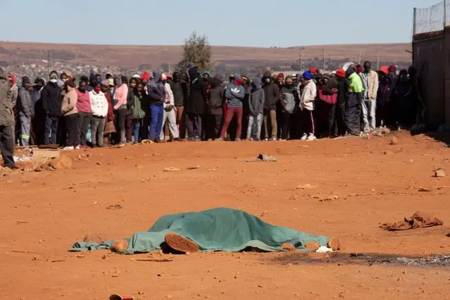 People look on a body of one of two looters, near a place where they died, in Johannesburg, South Africa, 13 July 2021. Former South Africa President Zuma was arrested on 07 July, and sentenced to 15 months in prison for contempt of court. Protests by his supporters included shops being looted, burned cars and the blocking of city streets in the country. (Photo by Kim Ludbrook/EPA/EFE)