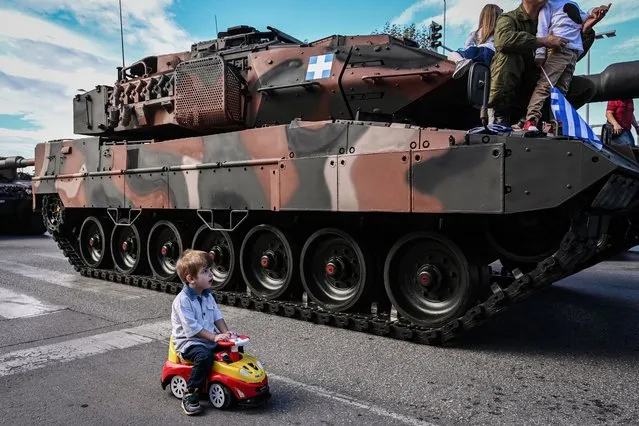 A child sits in his ride-on car next to a Hellenic Ground Forces' Leopard 2A6 HEL battle tank during a military parade to mark National “Oxi” (No) Day in Thessaloniki on October 28, 2023, commemorating Greece's refusal to accept the ultimatum given by fascist Italy in 1940 during World War II. (Photo by Sakis Mitrolidis/AFP Photo)