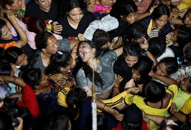 Women struggle as they compete to drink homemade alcohol poured from the mouth of an idol of “Swet Bhairab” during the annual Indra Jatra festival to worship Indra, Kumari and other deities and to mark the end of monsoon season in Kathmandu, Nepal on September 11, 2022. (Photo by Navesh Chitrakar/Reuters)